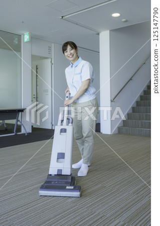 Portrait of a female cleaner vacuuming in an office building. Photo courtesy of Tokyo Electronics College, Denpa Gakuen School Corporation. 125147790