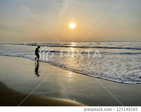 一個男孩在夕陽和平靜的水面上玩耍的剪影 125148185