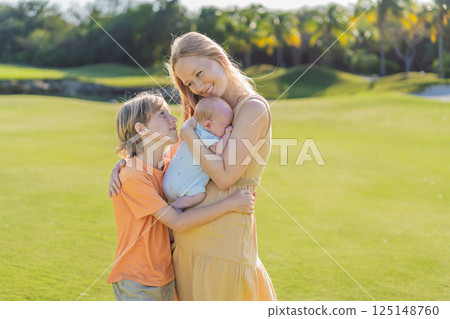 Mother, older son, and newborn baby on a meadow in the park. Family spending quality time together in nature. Parenthood, love, and family bond concept 125148760