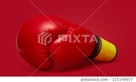 Single, vibrant red boxing glove with yellow and black wrist wrap against matching deep red background. Single, vibrant red boxing glove with yellow and black wrist wrap against matching deep red background. 125149057