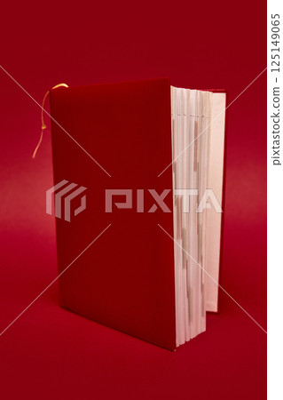 Red hardcover book with exposed pages standing vertically on rich red background. Red hardcover book with exposed pages standing vertically on rich red background. 125149065
