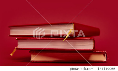 Stack of red hardcover books with golden ribbons arranged in minimalist composition on red background. Stack of red hardcover books with golden ribbons arranged in minimalist composition on red background. 125149066