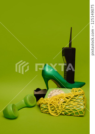 High heel, rotary phone and brick mobile phone arranged on green backdrop with tangled yellow mesh. High heel, rotary phone and brick mobile phone arranged on green backdrop with tangled yellow mesh. 125149075