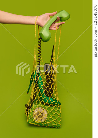 Green vintage telephone in yellow mesh bag with retro mobile phone and high heel against green background. Green vintage telephone in yellow mesh bag with retro mobile phone and high heel against green background. 125149076