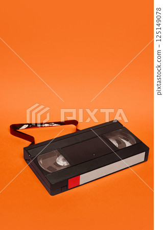 VHS cassette with part of tape unraveled on orange background. Decay of analog memory. Concept of retro aesthetics VHS cassette with part of tape unraveled on orange background. Decay of analog memory. Concept of retro aesthetics 125149078