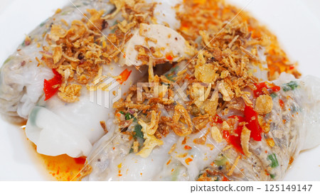 Close-up of a Vietnamese rice roll filled with pork and mushrooms, topped with fried garlic and chili oil. A vibrant, flavorful street food perfect for culinary content. 125149147