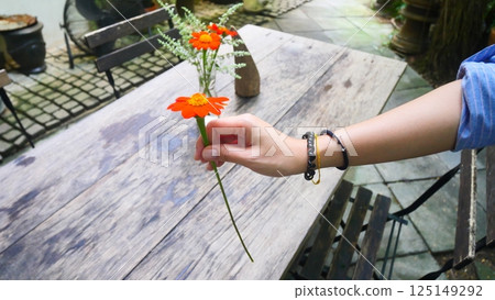 A hand is holding a flower with a cafe atmosphere in the background 125149292