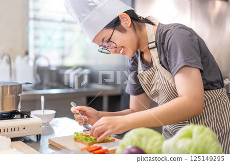 Smiling Young Female Chef Preparing a Sandwich in a Professional Kitchen Smiling Young Female Chef Preparing a Sandwich in a Professional Kitchen 125149295