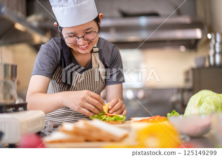 Smiling Young Female Chef Preparing a Sandwich in a Professional Kitchen Smiling Young Female Chef Preparing a Sandwich in a Professional Kitchen 125149299