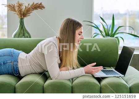 Young woman lying on sofa at home using laptop Young woman lying on sofa at home using laptop 125151659