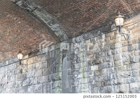 Two lantern lighting a spot on stone wall and red brick ceiling in tunnel under the high level bridge. Two lantern lighting a spot on stone wall and red brick ceiling in tunnel under the high level bridge. 125152003
