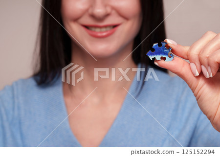 A smile of a girl holding a wooden blue puzzle in her hand. Advertising photo of unique puzzles. 125152294