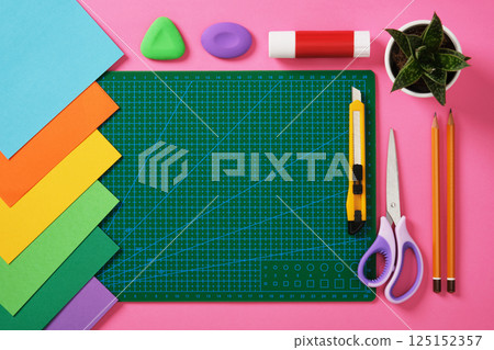 Supplies for paper art hobby: cutting mat, scissors, craft knife, pencil, eraser, glue colored paper on pink background. Place for your text. Paper crafts work table flatlay. 125152357