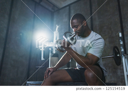 Fitness workout in gym. African American man bodybuilder picking up dumbbells in gym. Workout weight training biceps muscles with dumbbell in fitness club. Man doing sports exercise. Healthy lifestyle 125154519
