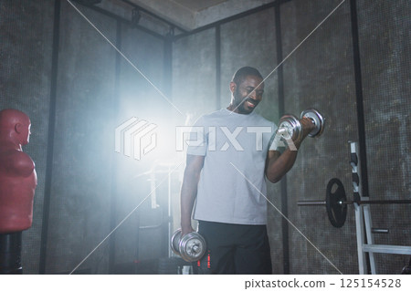 Fitness workout in gym. African American man bodybuilder picking up dumbbells in gym. Workout weight training biceps muscles with dumbbell in fitness club. Man doing sports exercise. Healthy lifestyle Fitness workout in gym. African American man bodybuilder picking up dumbbells in gym. Workout weight training biceps muscles with dumbbell in fitness club. Man doing sports exercise. Healthy lifestyle 125154528