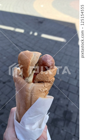 A person holding a hot dog with mustard 125154555