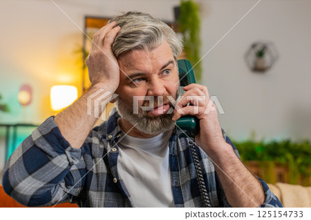 Sad disinterested senior man talking on vintage retro wired telephone with hotline helpline service 125154733