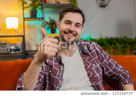 Happy man looking approvingly at camera showing double thumbs up like sign positive feedback at home 125154737