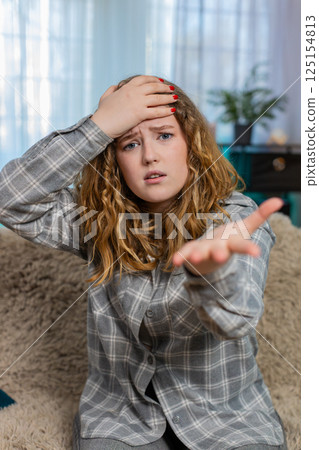 Woman sits on sofa making facepalm gesture feeling disappointed frustrated after unexpected failure Woman sits on sofa making facepalm gesture feeling disappointed frustrated after unexpected failure 125154813