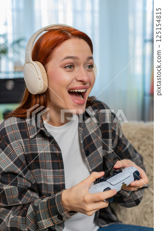 Young woman on sofa playing video game with joystick emotionally reacting to action on screen Young woman on sofa playing video game with joystick emotionally reacting to action on screen 125154815