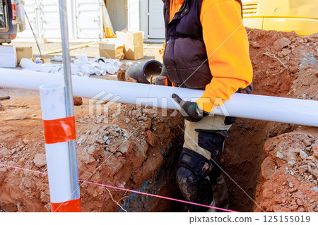 Worker carefully cutting plumbing pvc pipes in trench to sewer lines system at construction site 125155019