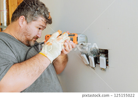 Professional electrician on installing electrical switches in wall during home improvement works 125155022