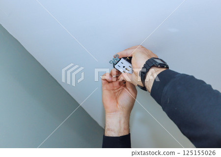 Electrician worker installs ceiling outlet, prioritizing safety, proper connections. 125155026