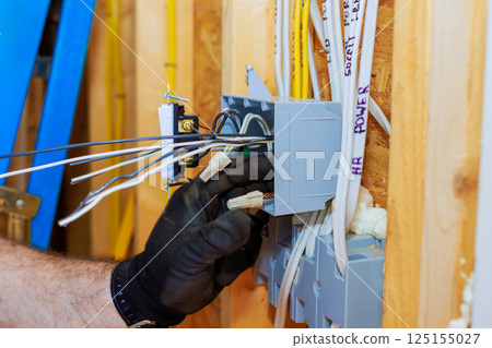 An electrician connects wires to junction box while installing electrical systems in new home. An electrician connects wires to junction box while installing electrical systems in new home. 125155027