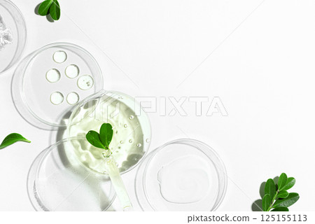 Bio laboratory with green plant leaves,  dropper and cosmetic gel swatches on white background 125155113