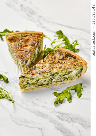 Delicious spinach and feta quiche slices with fresh arugula on marble 125155148