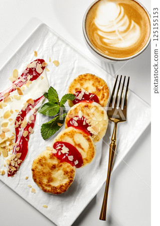 Cottage cheese pancakes, syrniki, with raspberry jam, sour cream and almond flakes, served with cappuccino 125155153