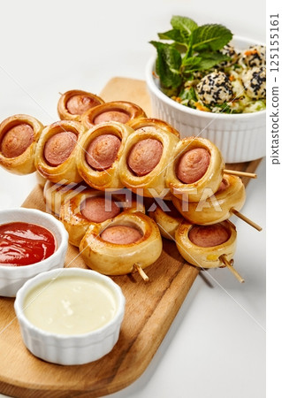 Sausage rolls skewers with dipping sauces and sesame salad on white background 125155161
