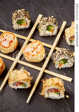 Variety of sushi rolls forming a tic-tac-toe game with chopsticks on dark background Variety of sushi rolls forming a tic-tac-toe game with chopsticks on dark background 125155168