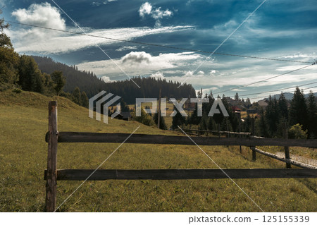 In this calm countryside setting, a simple wooden fence leads toward a home nestled on a hill. 125155339