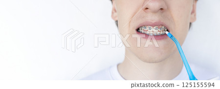 A young unrecognizable man with braces cleaning his teeth with oral irrigator. 125155594