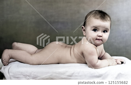 Vintage portrait of a cute little girl. Six-month naked baby lies on her stomach and looks attentively. Retro photo from 1967. 125155682