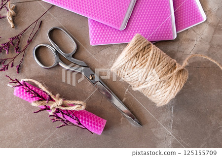 Crafting materials with pink wax sheets, scissors, jute twine, and dried flowers on stone surface 125155709