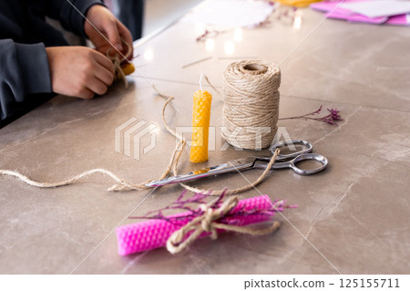 Young hands crafting beeswax candle with natural twine on marble surface Young hands crafting beeswax candle with natural twine on marble surface 125155711