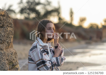 A young girl is sitting on the beach in a checkered shirt A young girl is sitting on the beach in a checkered shirt 125156700