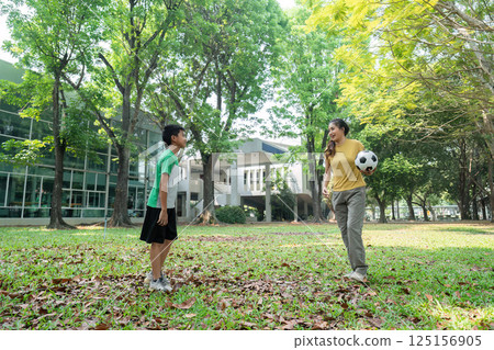 Playful Interaction and Soccer Fun. A young boy and woman enjoying a game of soccer in a park. 125156905