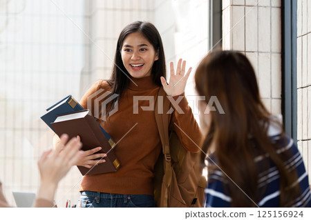 Friendly Greetings and Books. A student waves happily, carrying books and sharing excitement with friends. Friendly Greetings and Books. A student waves happily, carrying books and sharing excitement with friends. 125156924