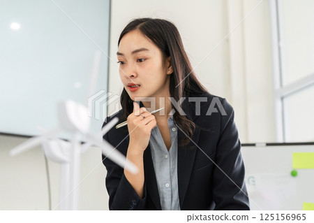 Strategic Planning in Sustainability. A businesswoman contemplating sustainable energy solutions with a wind turbine model. 125156965
