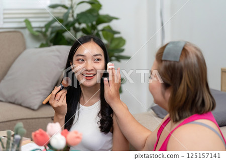 Makeup and Learning. A woman enthusiastically teaching her friend makeup techniques in a comfortable home environment. 125157141