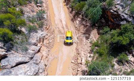 Yellow suv navigating muddy off-road trail in rocky terrain. 125157719