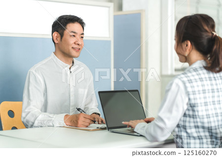 A male customer at the reception desk and a female office staff member handling the customer service 125160270