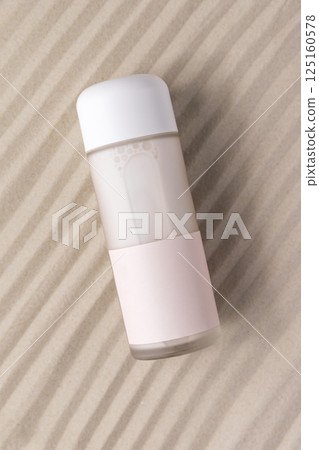 Moisturizing cosmetic milk in glass packaging on sand, empty label, minimalist design 125160578