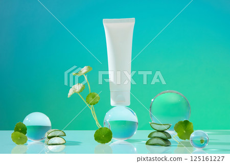 Unlabeled cream tube stand on a glass ball. Gotu kola plants with long stems and green leaves. Aloe vera cut into pieces, stacked and placed around. Laboratory concept with cosmetic ingredients 125161227