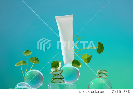 An unlabeled tube of cream stands on a square glass pedestal. The tube leans against a glass ball. The small glass ball stacked on top of the larger one, with a green pennywort leaf for decoration. An unlabeled tube of cream stands on a square glass pedestal. The tube leans against a glass ball. The small glass ball stacked on top of the larger one, with a green pennywort leaf for decoration. 125161228