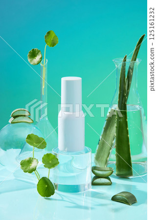 Vertical photo of a white plastic cosmetic bottle, without a label for advertising. Aloe vera placed upright in a glass measuring flask. Centella asiatica is scattered around the laboratory jars. 125161232