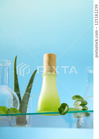 Vertical photo of cylindrical plastic jars with wooden lids placed on glass surface with ingredients like aloe vera and pennywort. Laboratory glass jars containing clear liquids. Blue background. Vertical photo of cylindrical plastic jars with wooden lids placed on glass surface with ingredients like aloe vera and pennywort. Laboratory glass jars containing clear liquids. Blue background. 125161239